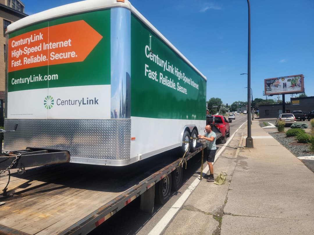 Flatbed tow truck transporting a box truck along city roadway
